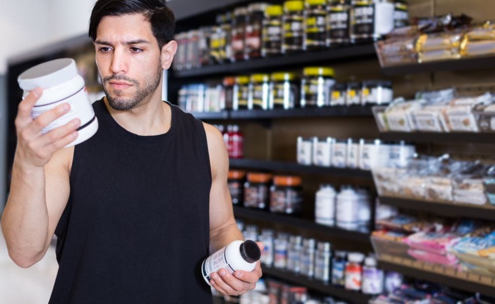 Man choosing between supplements at nutrition store.