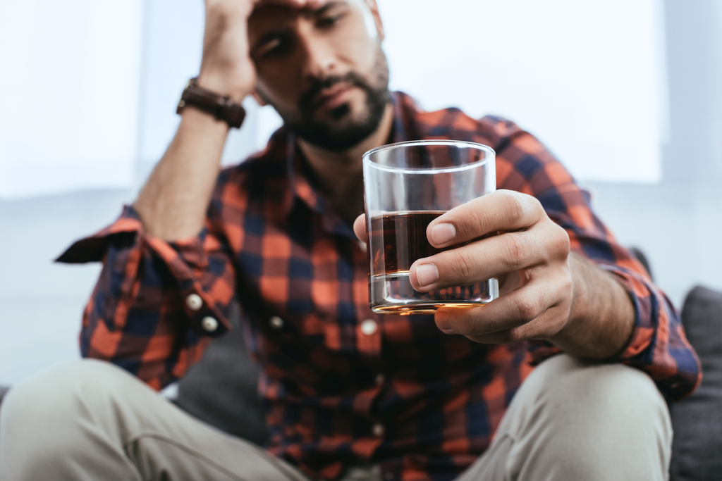 Sad-looking man holding glass of whiskey