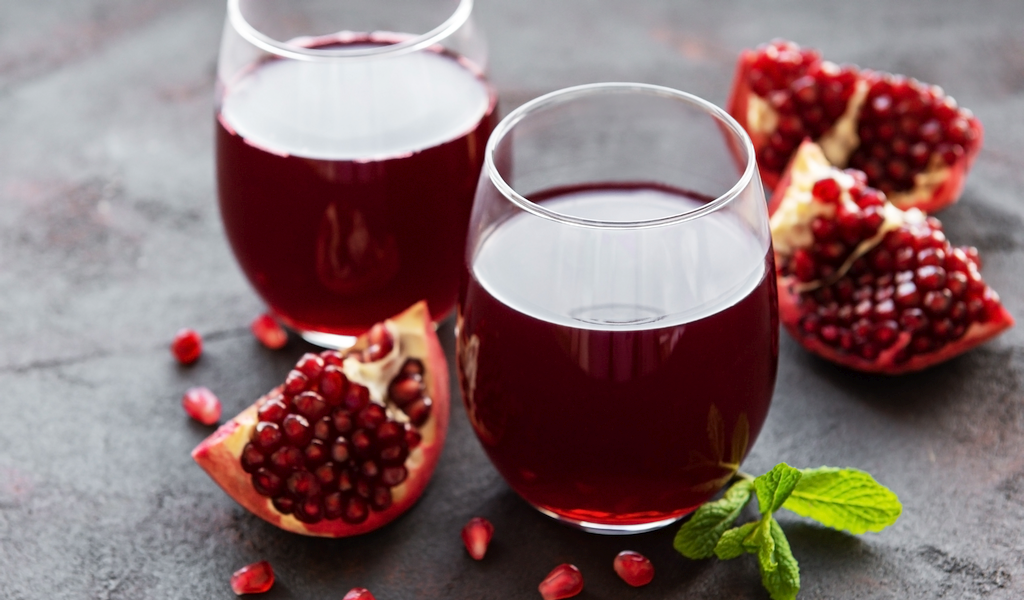 Two glasses of pomegranate juice next to sliced pomegranate.