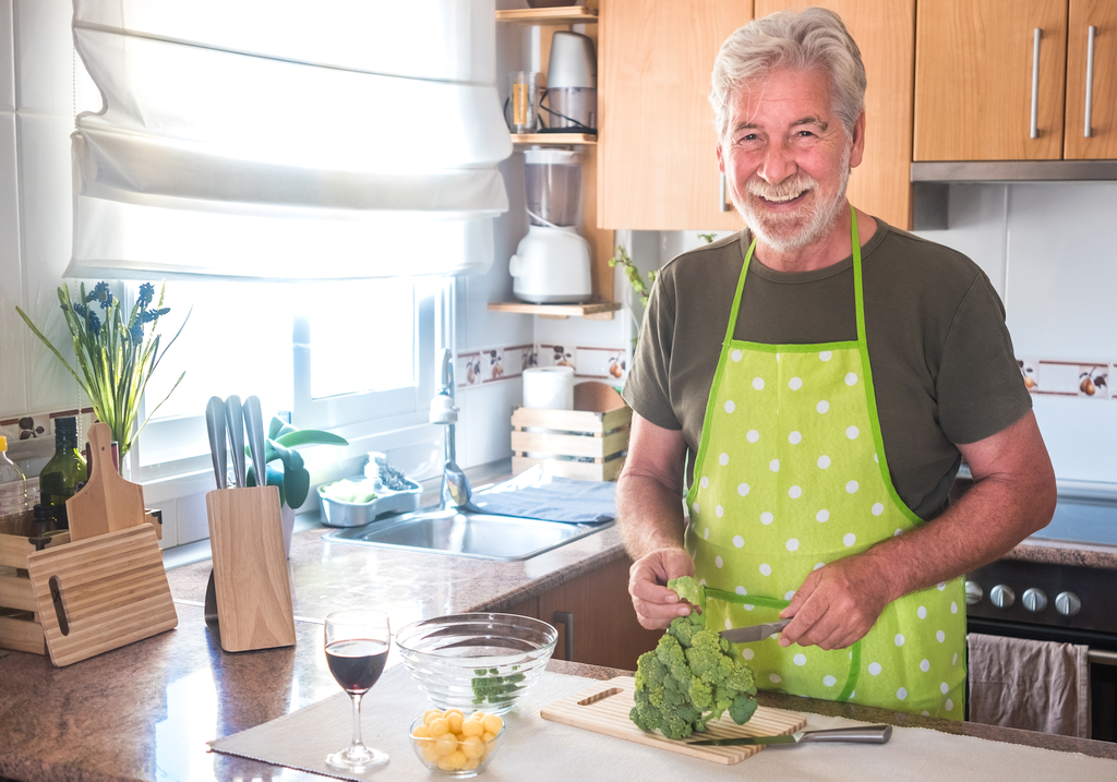 Older man in kitchen chopping broccoli and other foods for prostate health