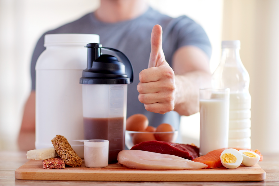 Man standing behind large selection of protein -rich foods giving thumbs up