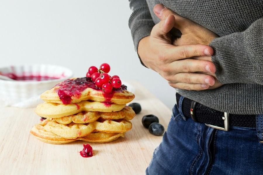 Man holding his stomach hungrily next to a plate of waffles with syrup